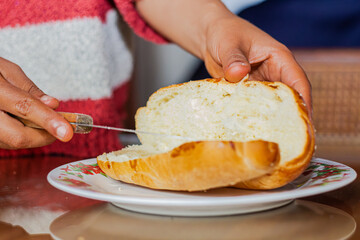 hands of female baker spreading butter on an open loaf with a knife on a plate at a breakfast table