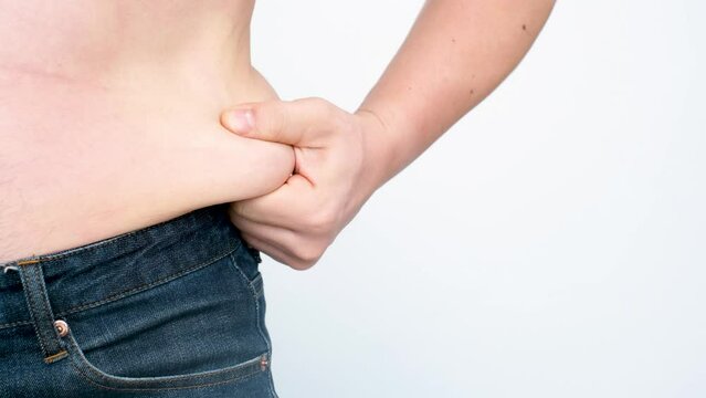 A male hand holding excessive belly fat on white background, overweight concept.