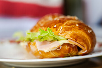 baker's hand showing a sandwich with open bread with cheese ham lettuce and mayonnaise on a plate on a table for breakfast