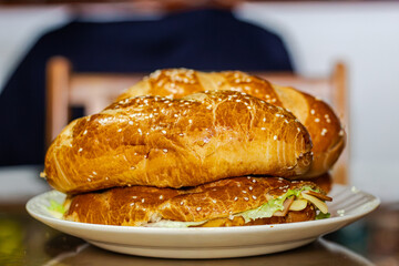 baker's hand showing a sandwich with open bread with cheese ham lettuce and mayonnaise on a plate on a table for breakfast