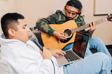 Guitarist and singer using laptop sitting on the sofa playing
