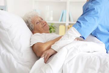 Female nurse putting senior woman to bed in bedroom