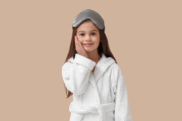 Cute little happy girl in bathrobe with sleeping mask on beige background