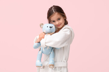Cute little happy girl in bathrobe with teddy bear on pink background