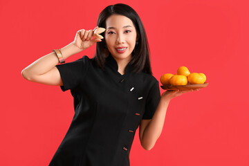 Young Asian woman with fortune cookie and mandarins on red background. Chinese New Year celebration