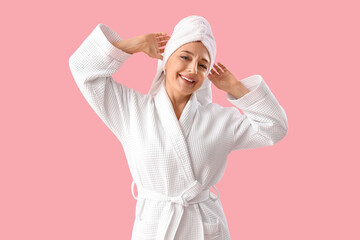 Mature woman in bathrobe after shower on pink background