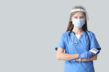 Beautiful doctor in protective masks with infrared thermometer on light background