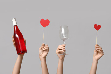 Female hands holding bottle of wine, glass and paper hearts on grey background. Valentine's Day...