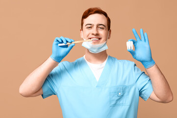 Male dentist with toothbrush and tooth model on beige background. World Dentist Day