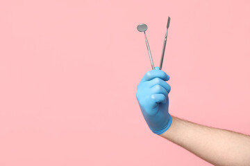 Male dentist hand holding dental tools on pink background. World Dentist Day