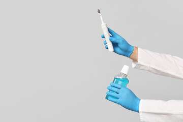 Dentist hands with electric toothbrush and bottle of mouth rinse on grey background. World Dentist Day