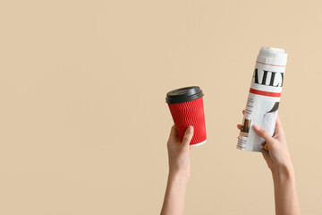 Woman with rolled newspaper and coffee cup on beige background