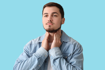 Young man with thyroid gland problem on blue background