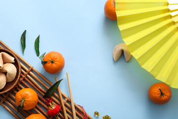 Composition with paper fan, bamboo mat, tangerines and fortune cookies on blue background. Chinese...
