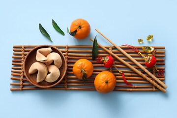 Composition with bamboo mat, tangerines and fortune cookies on blue background. Chinese New Year...