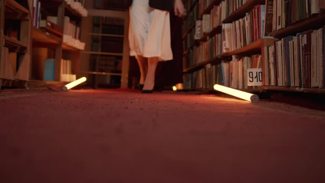 Women are mysteriously walking in library. Stock footage. Secret sorority in night library. Elegant women mysteriously gather in night library with flashing light