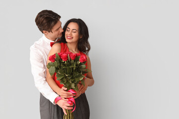 Young couple with roses on light background. Valentine's Day celebration