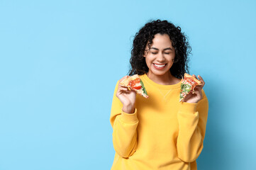 Beautiful young happy African-American woman with slices of delicious pizza on blue background