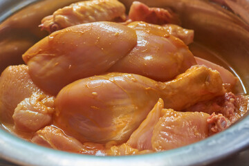 close-up of marinated skinless chicken meat, uncooked seasoned raw legs, wings and thigh in a bowl...