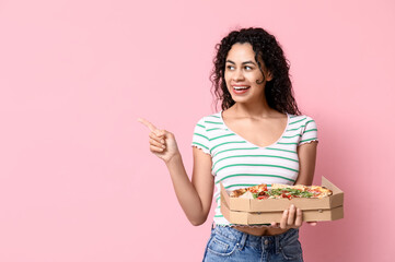 Beautiful young happy African-American woman with delicious pizza pointing at something on pink...