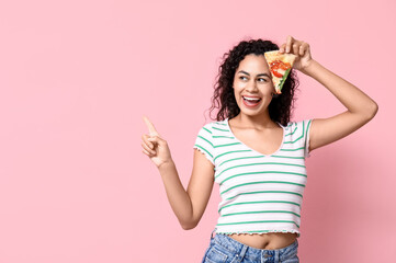 Beautiful young happy African-American woman with slice of delicious pizza pointing at something on pink background