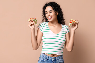 Beautiful young happy African-American woman with slices of delicious pizza on beige background
