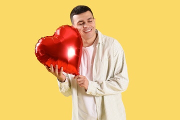 Young man with heart-shaped balloon on yellow background. Valentine's Day celebration