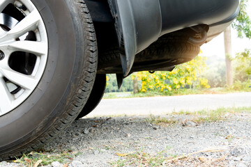 Partial view of a car wheel and tire from the rear. The undercarriage of the car. Parked on a rocky...