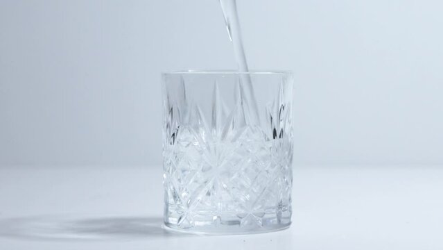 clear liquid water being poured into embossed rocks drinking glass