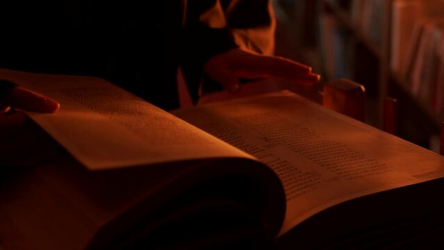 Man reading large mysterious book. Stock footage. Close-up of mysterious man reading ancient forbidden book in library. Secret society with books in night library