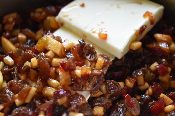 Adding butter to cooking mincemeat. a mix of small pieces of dried fruit, fresh apples, and orange peel, spices, sugar and brandy.