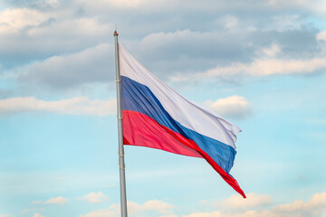 Russian tricolor flag waving in the wind against a blue sky.