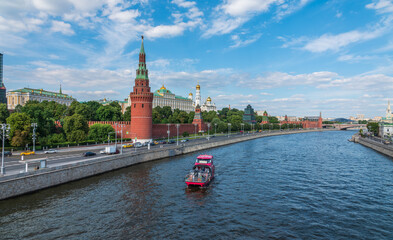 View of Kremlin with Vodovzvodnaya tower, Grand Kremlin Palace from repaired Bolshoy Kamenny Bridge in Moscow city on sunny summer day. Cruise ship sails on the Moscow river