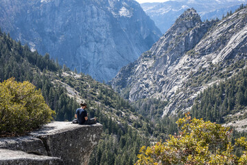 Man with hat sitting on the edge of cliff in the nature outdoor adventure yosemite national park nevada fall john muir trail
