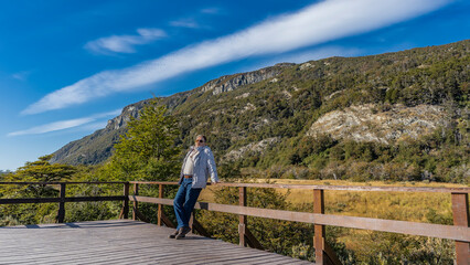 Fototapeta na wymiar The landscape of Patagonia. A mountain overgrown with green vegetation, against a blue sky, clouds. A man is standing on a wooden observation deck, leaning against the railing. Resting. Argentina.