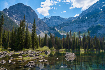 Incredibly beautiful transparent, emerald calm lake with reflection of rocky mountain on the Black Prince Cirque Trail. Majestic Canadian mountains with snow on sunny summer day in Alberta, Kananaskis