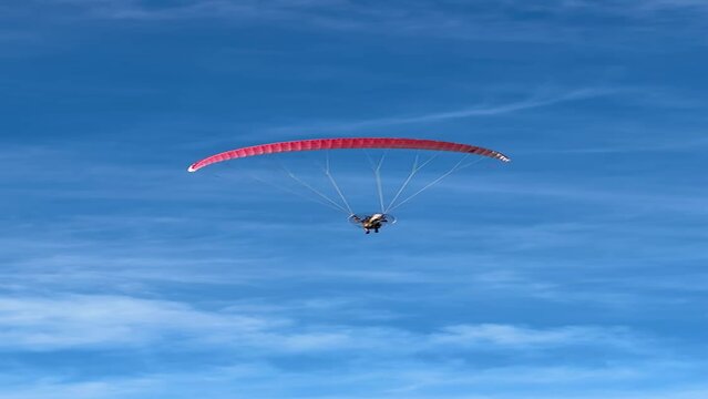 A person soaring over the city on a paramotor, a motorized paraglider. A vast blue sky in the background.