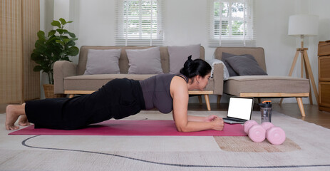 Fat Asian woman stretching at home on a fitness mat. Practicing activities at home online exercise classes Practice stretching on your yoga mat at home to stay healthy and in shape.