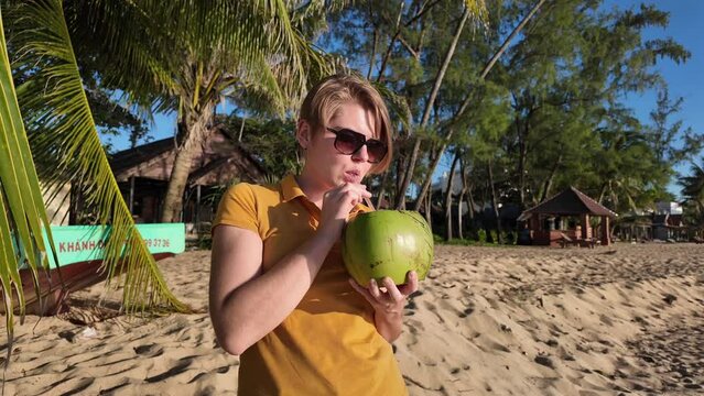 A person is sipping from a coconut on a sunny beach, depicting a tropical vacation concept