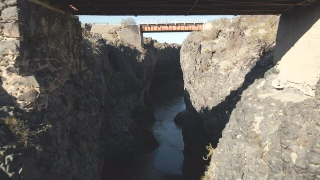 Drone flying beneath the bridge at "La Pasarela," a magnificent spot near Bardas Blancas, Mendoza, Argentina, capturing the breathtaking scenery.