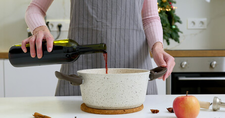 Woman is pouring red wine to the pot