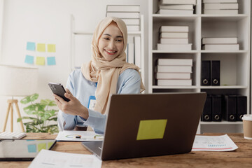 Beautiful Asian Muslim businesswoman uses smartphone to view social media application Answer chats with customers or discuss business transactions.