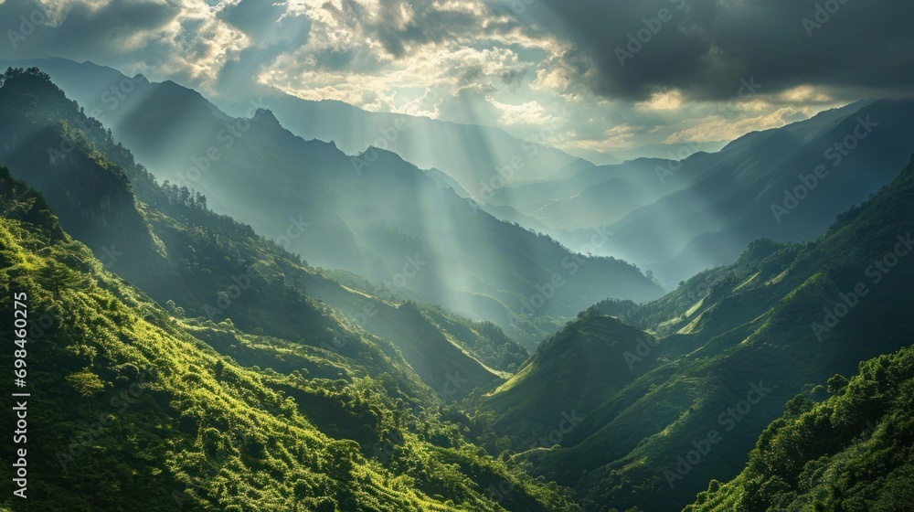 Wall mural the sun shines through the clouds over a valley with lush green hills in the foreground and a mounta