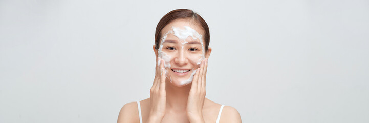 Happy laughing young asian woman washing face with foam soap cosmetic product. Web banner