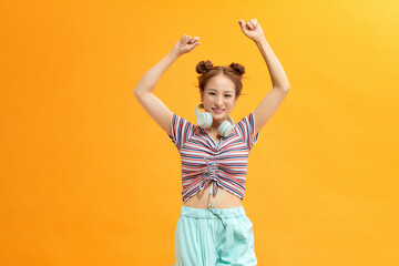 Girl dancing on yellow background wearing headphones on neck, lifestyle concept, copy space