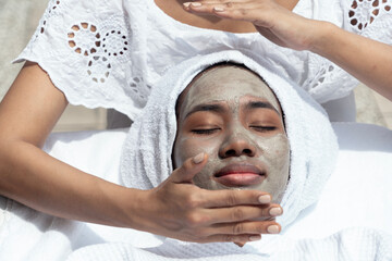 young black woman with her hair wrapped in a towel lies down and relaxes at a facial spa, gives a...