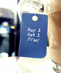 Blue tag hanging on coffee cup with text written BUY 1 GET 1 FREE, common form of sales promotion-...