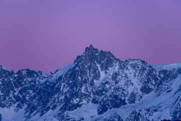 The Aiguille du Midi in the Mont Blanc massif with purple colors in Europe, France, Rhone Alpes, Savoie, Alps, in winter on a sunny day.