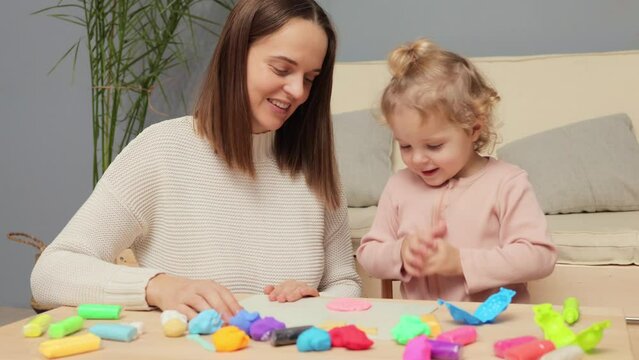 Modeling with children. Hands-on creativity. Playful plasticine activity. Happy positive Caucasian kid girl and mother playing colorful clay plasticine together in home interior