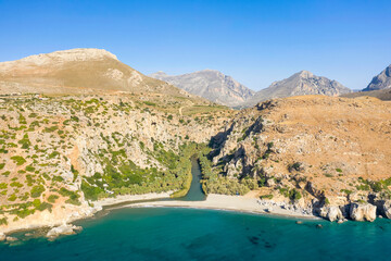 The sandy beach at the foot of the mountain next to a green palm grove , in Europe, Greece, Crete, Preveli, By the Mediterranean Sea, in summer, on a sunny day.